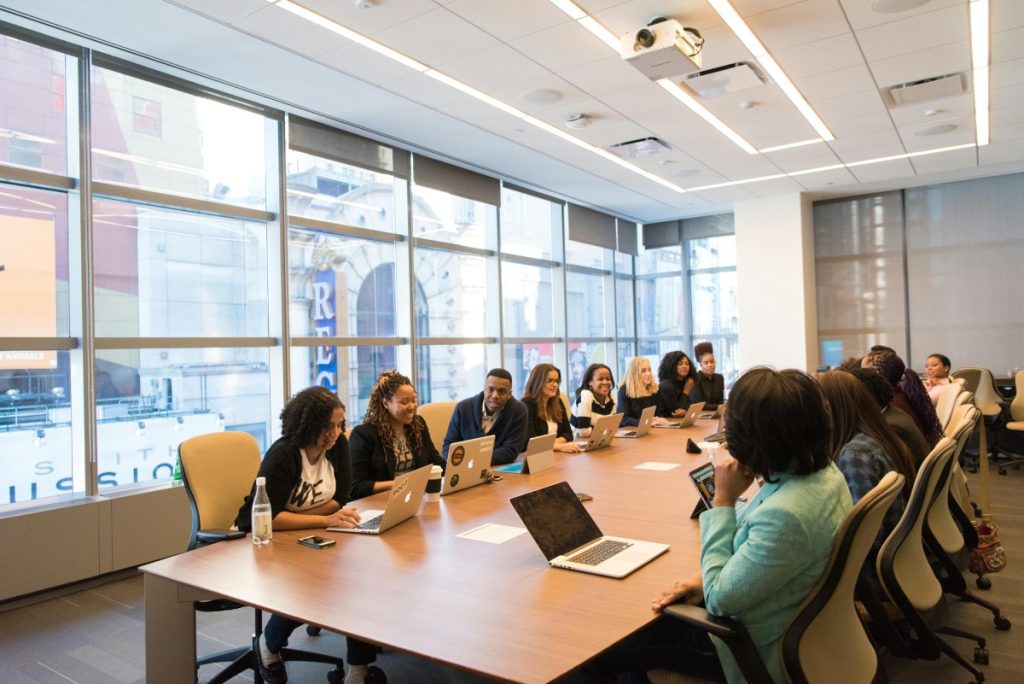  Groupe de personnes en réunion dans une salle de conférence moderne, assis autour d'une grande table avec des ordinateurs portables, échangeant des idées dans une ambiance professionnelle et collaborative.