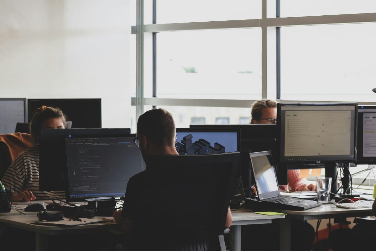 Groupe d'ingénieurs de prompt travaillant dans un open space, concentrés sur leurs écrans où s'affichent du code et des interfaces de développement